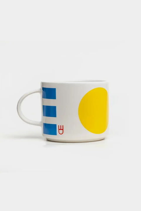 Eine weiße Tasse mit gelben und grünen Punkten sowie roten und blauen Linien