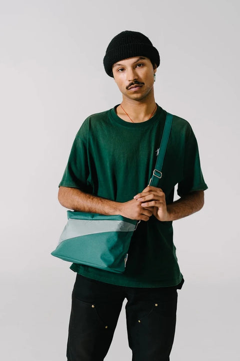 Eine Person trägt die New Bum Bag in Grün und Grau als Crossbody-Tasche.